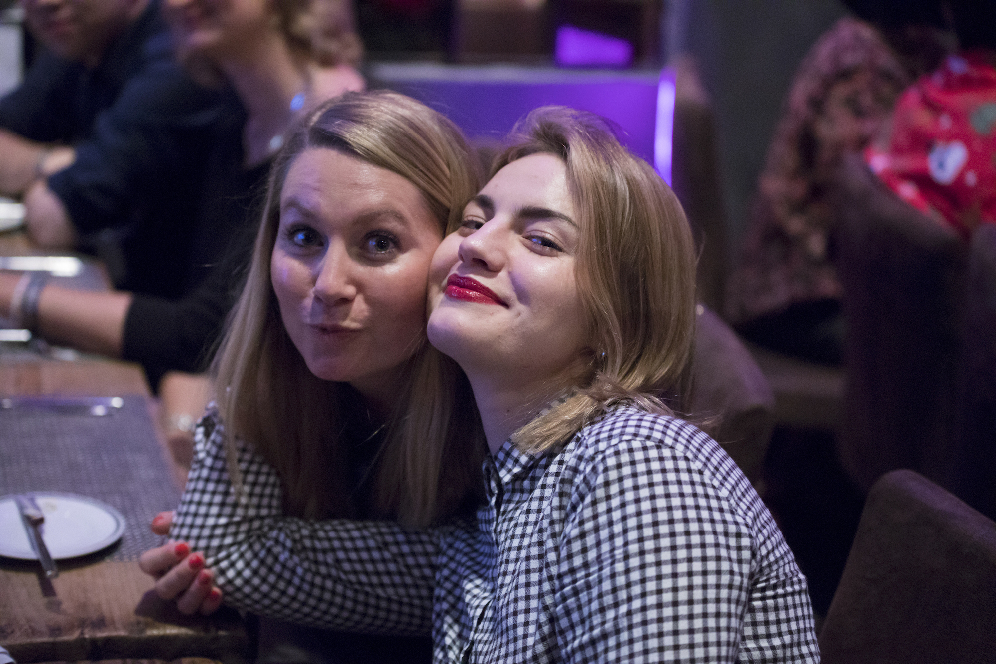 Zwei junge Frauen posieren gemeinsam vor der Kamera an einem Esstisch
